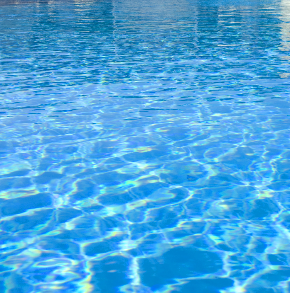 Sparkling pool water under the glistening sunlight, with rippling waves and a crystal-clear surface, inviting for a refreshing swim on a bright and sunny day.