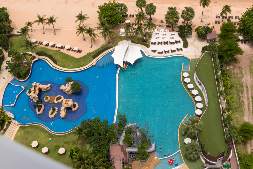 An aerial view of a lagoon-inspired swimming pool, with its curvaceous shape, sandy beach entry, lush landscaping, and turquoise water, reminiscent of a tropical paradise.