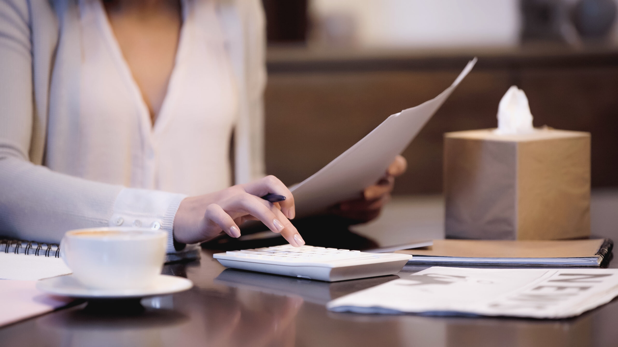 A woman seated at a desk with a budgeting spreadsheet and calculator, engaged in financial planning and budget management.