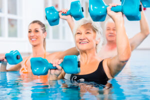 People young and senior in water gymnastics physiotherapy with dumbbells