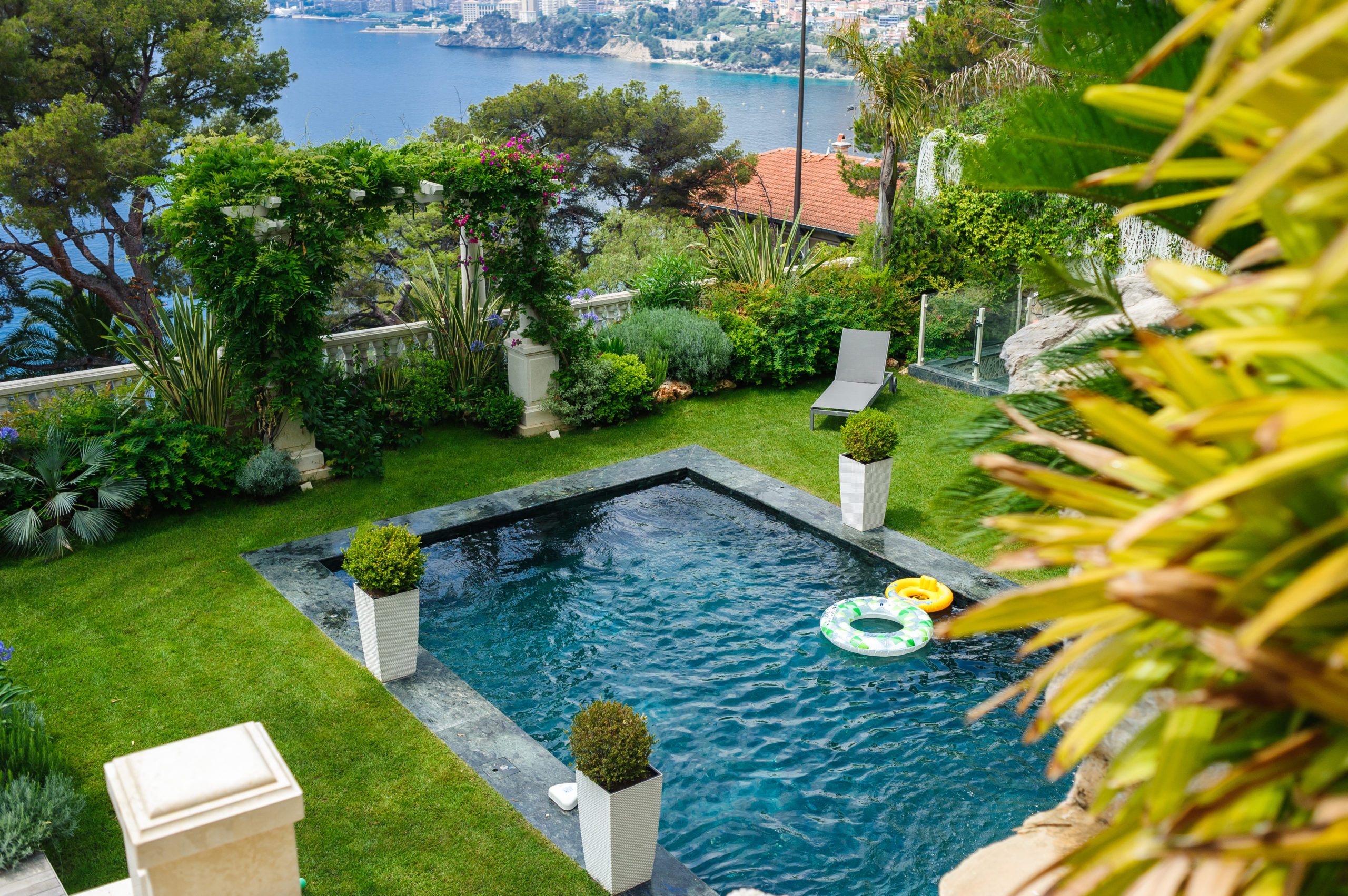 A pool with a lifebuoy floating in the water, surrounded by an abundance of lush plants and greenery, providing both safety and a natural, inviting ambiance.