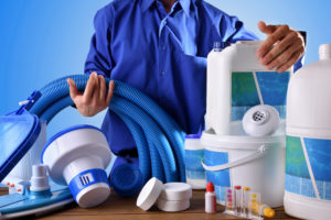 Swimming pool maintenance worker with chemical cleaning products and tools on wood table and blue background. Horizontal composition. Front view