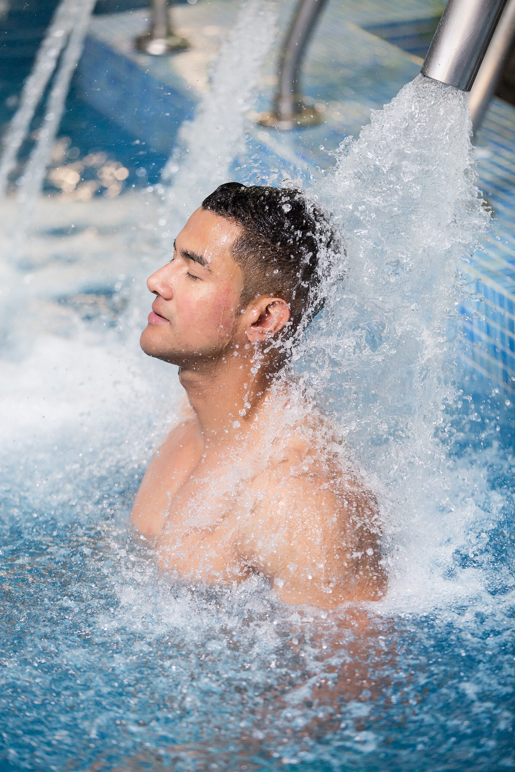 A man experiencing integrated hydrotherapy in a pool with soothing waterfalls, enjoying the therapeutic benefits of the cascading water for relaxation and well-being.