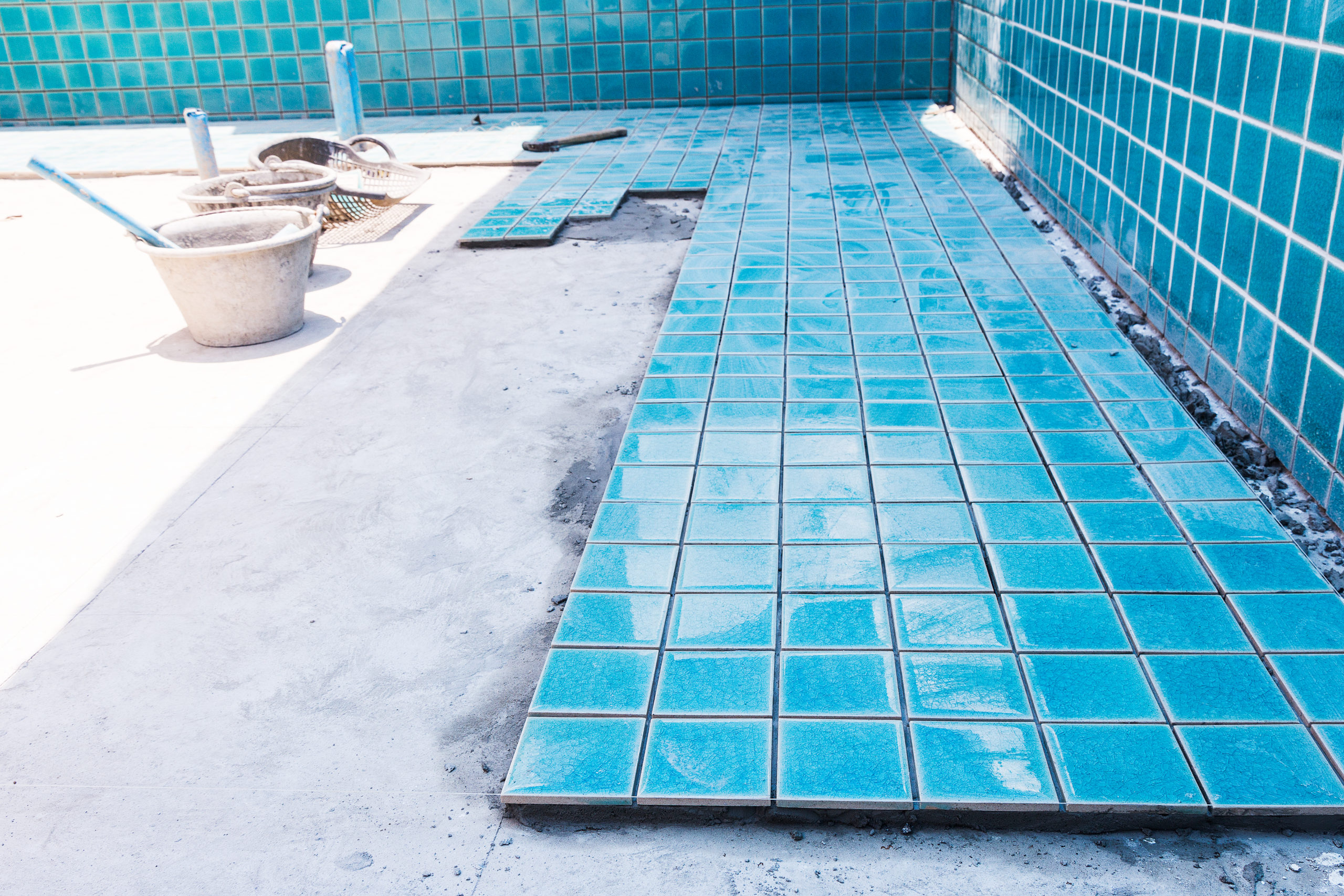 Workers are in the process of laying tiles on the pool floor, carefully aligning and setting them to create a durable and visually appealing surface for the pool.