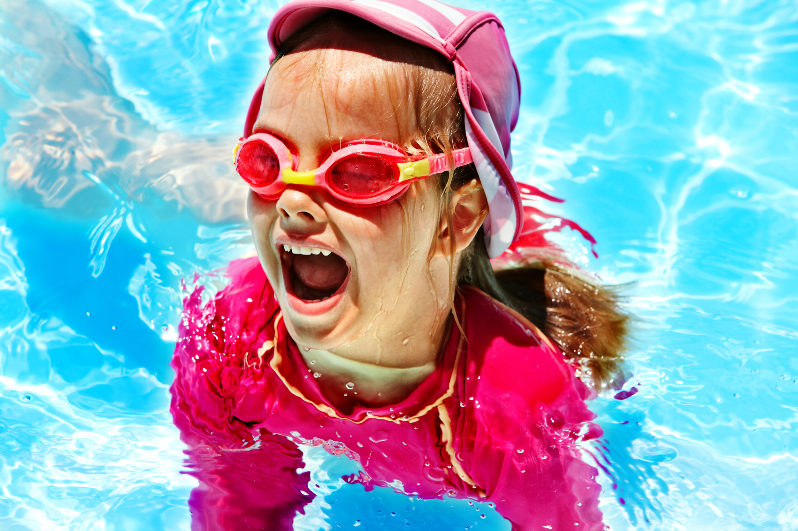 A happy child in a pool, smiling and enjoying a playful and joyful moment in the water.