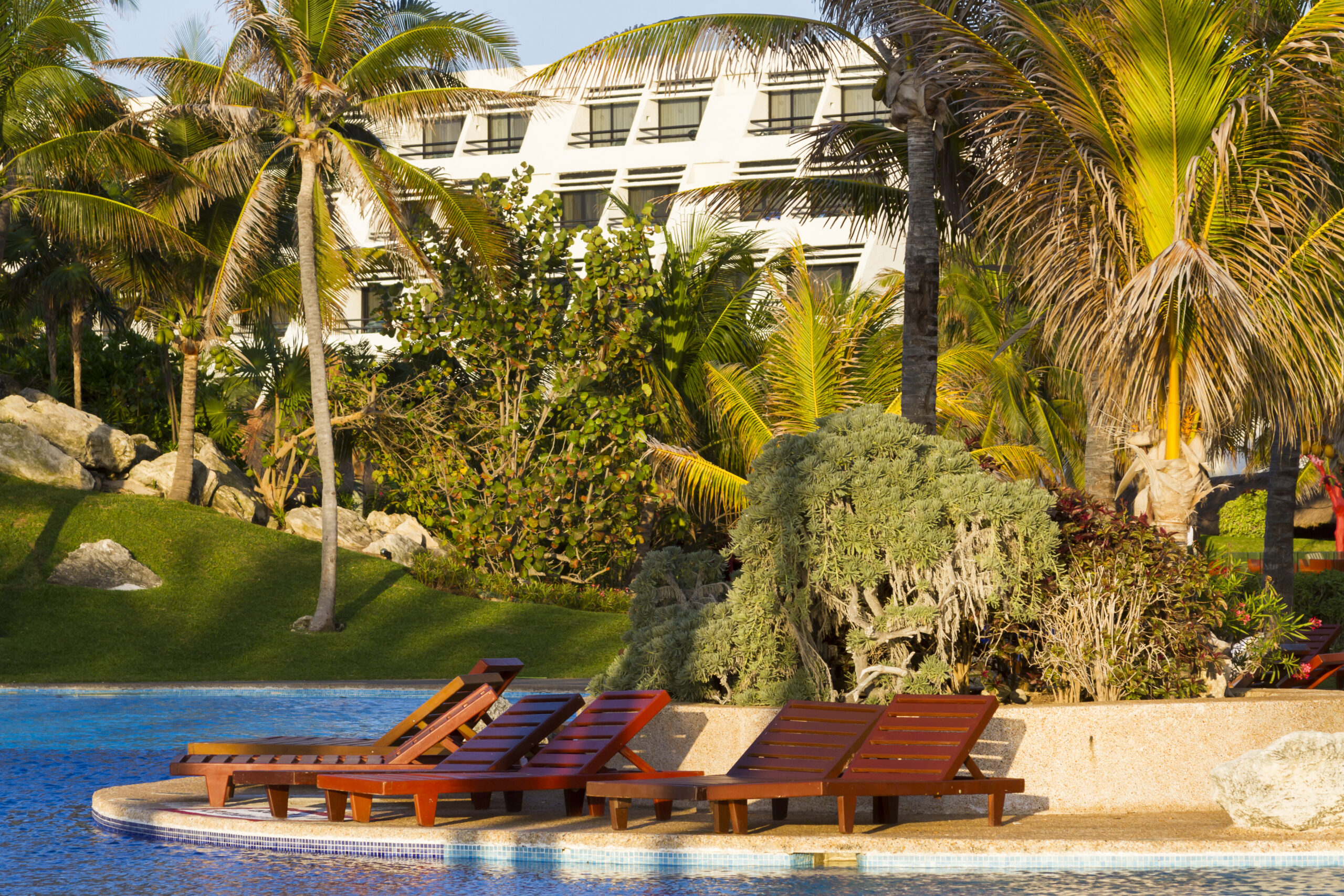 Poolside area with wooden chairs and a comfortable bed or lounger.