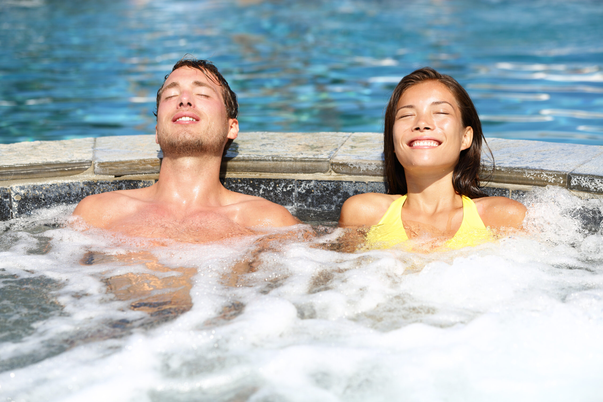 A man and a woman relaxing in hot tubs by the pool, enjoying a serene and luxurious poolside design for relaxation and leisure.