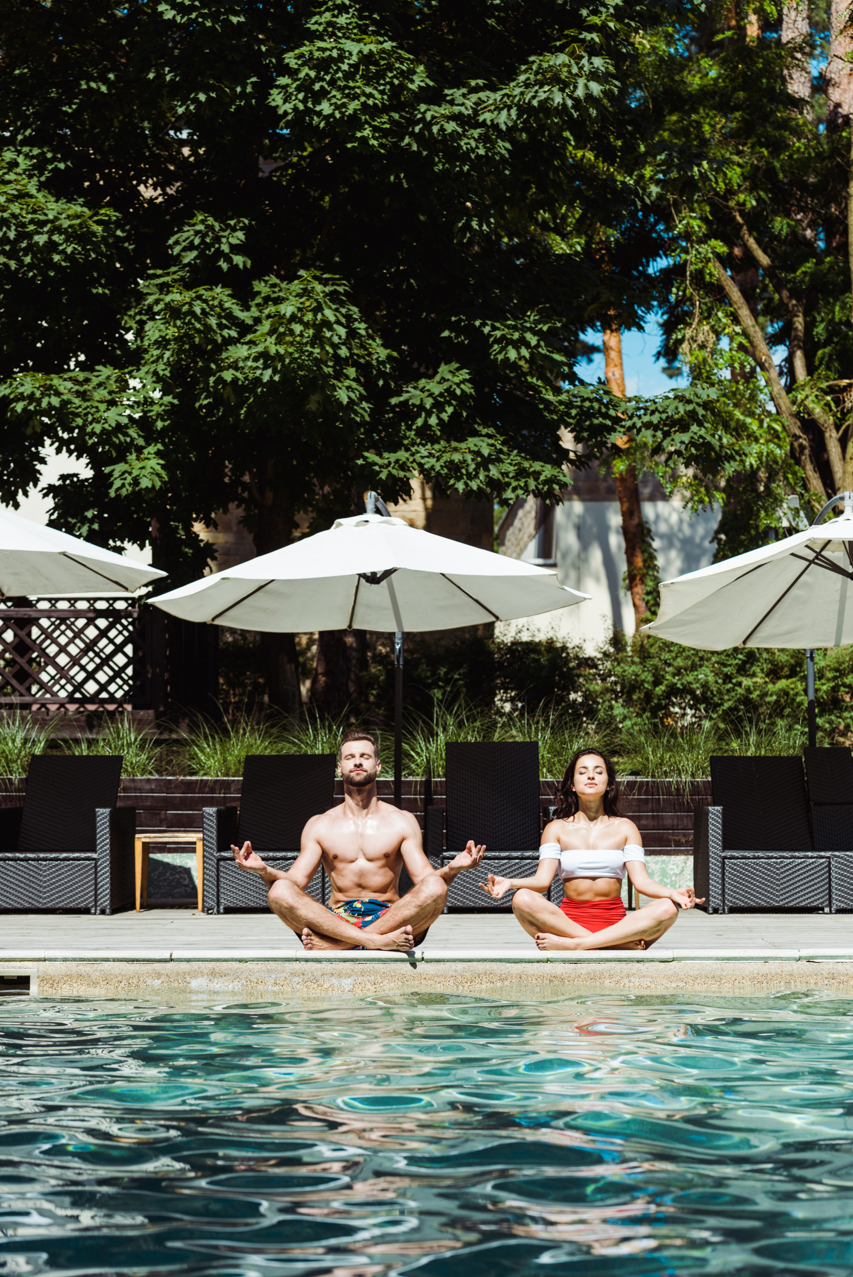 A man and a woman practicing yoga at the edge of the pool, combining relaxation and fitness in a serene poolside setting.