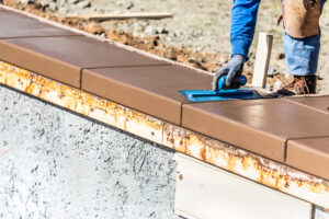 Construction Worker Using Trowel On Wet Cement Forming Coping Around New Pool.