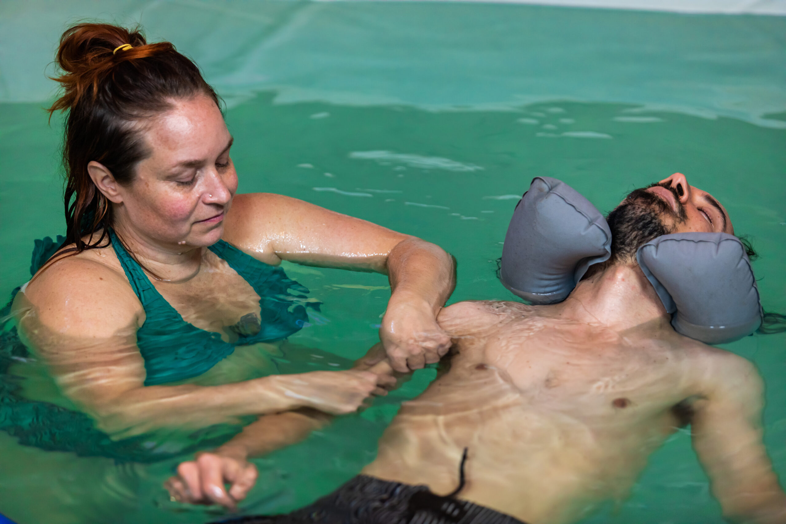 A hydrotherapy pool scene with a woman assisting a man, showcasing a therapeutic environment designed for rehabilitation and relaxation.