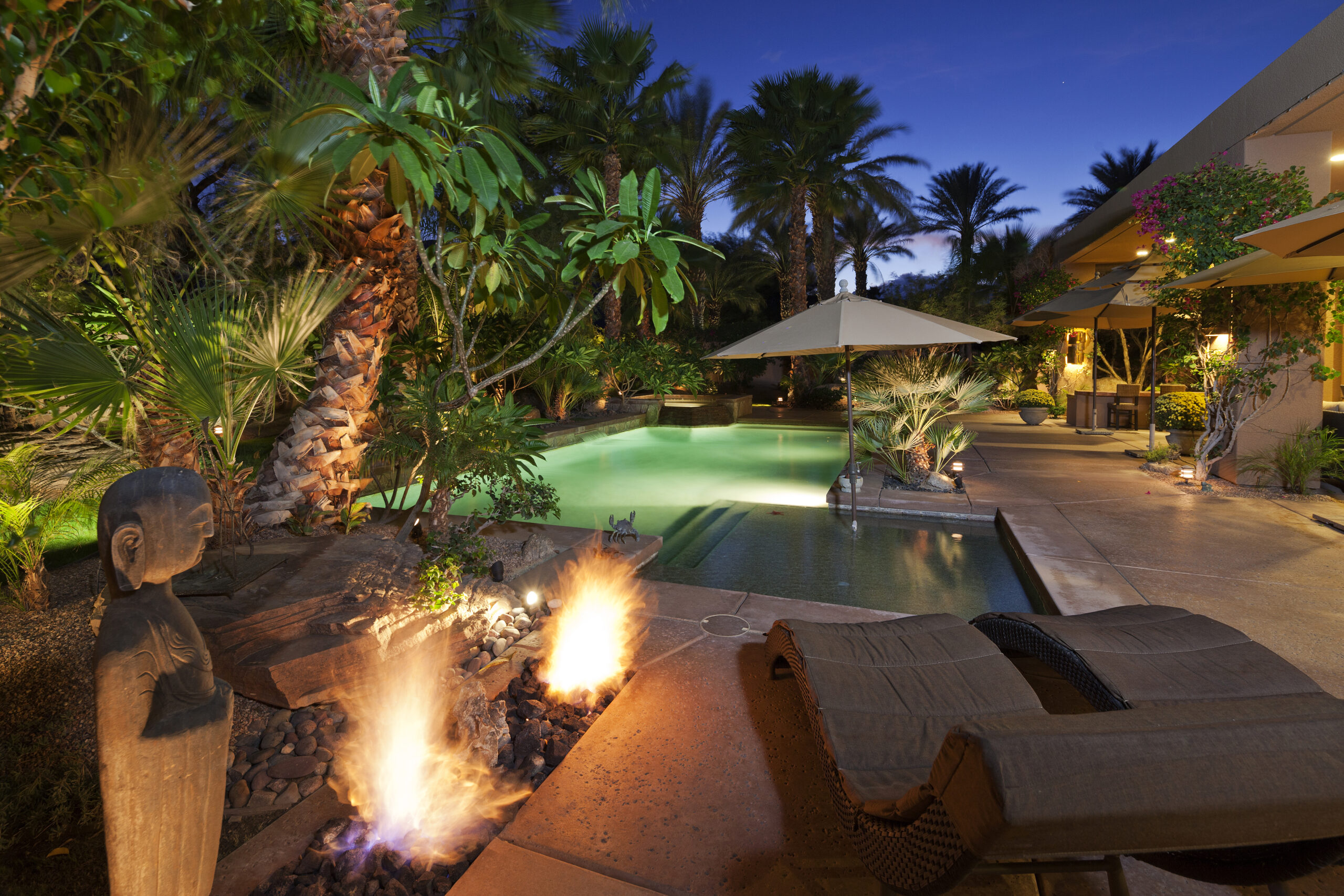 A pool surrounded by trees and chairs, with two fire pits on the side