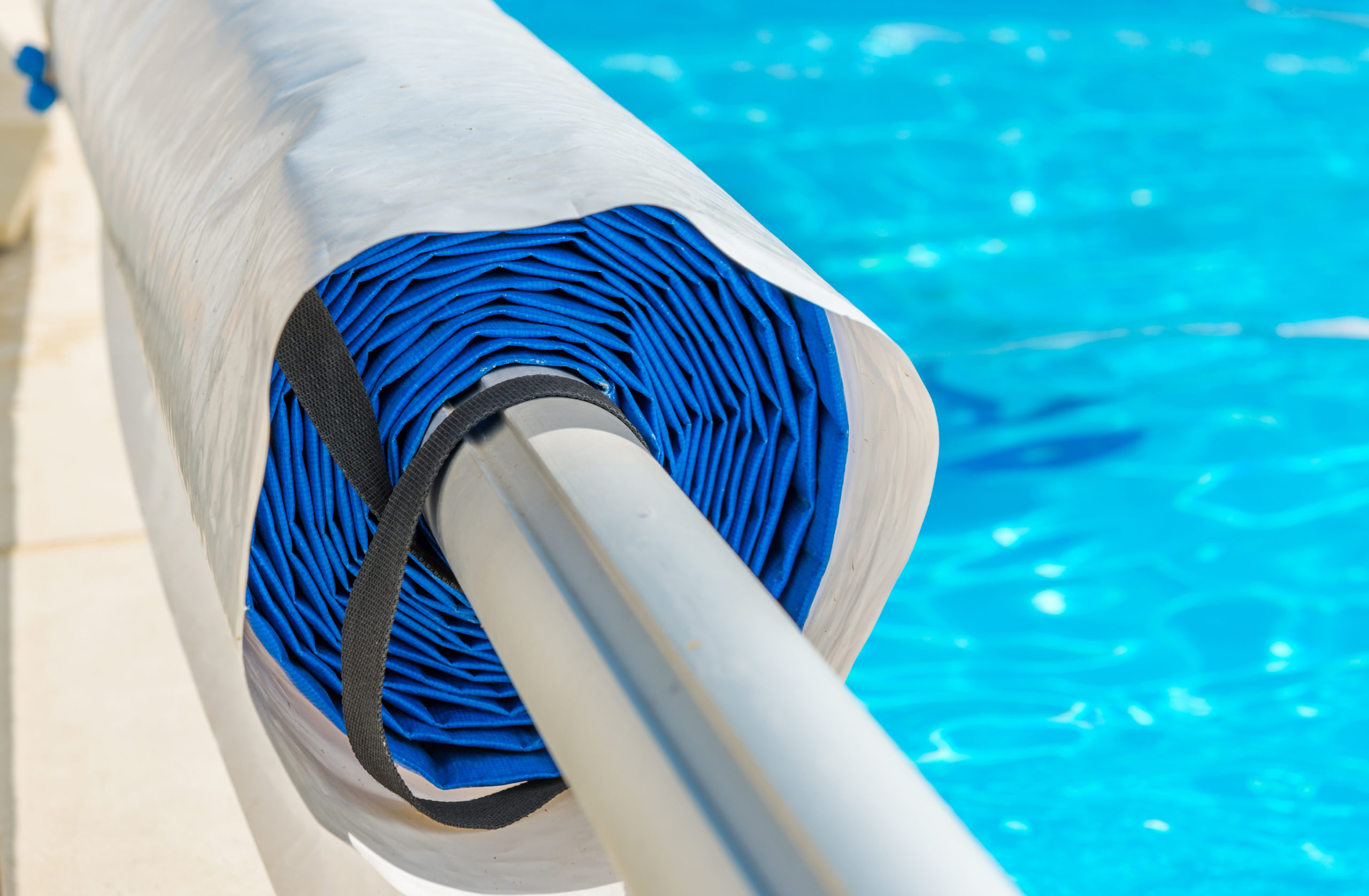 A rolled pool cover neatly stored at the edge of a swimming pool, ready to be unrolled for pool protection and maintenance.