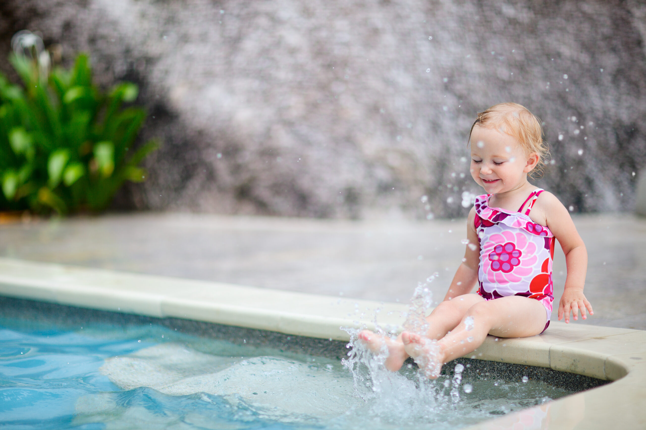A baby joyfully splashing water using her feet in a pool