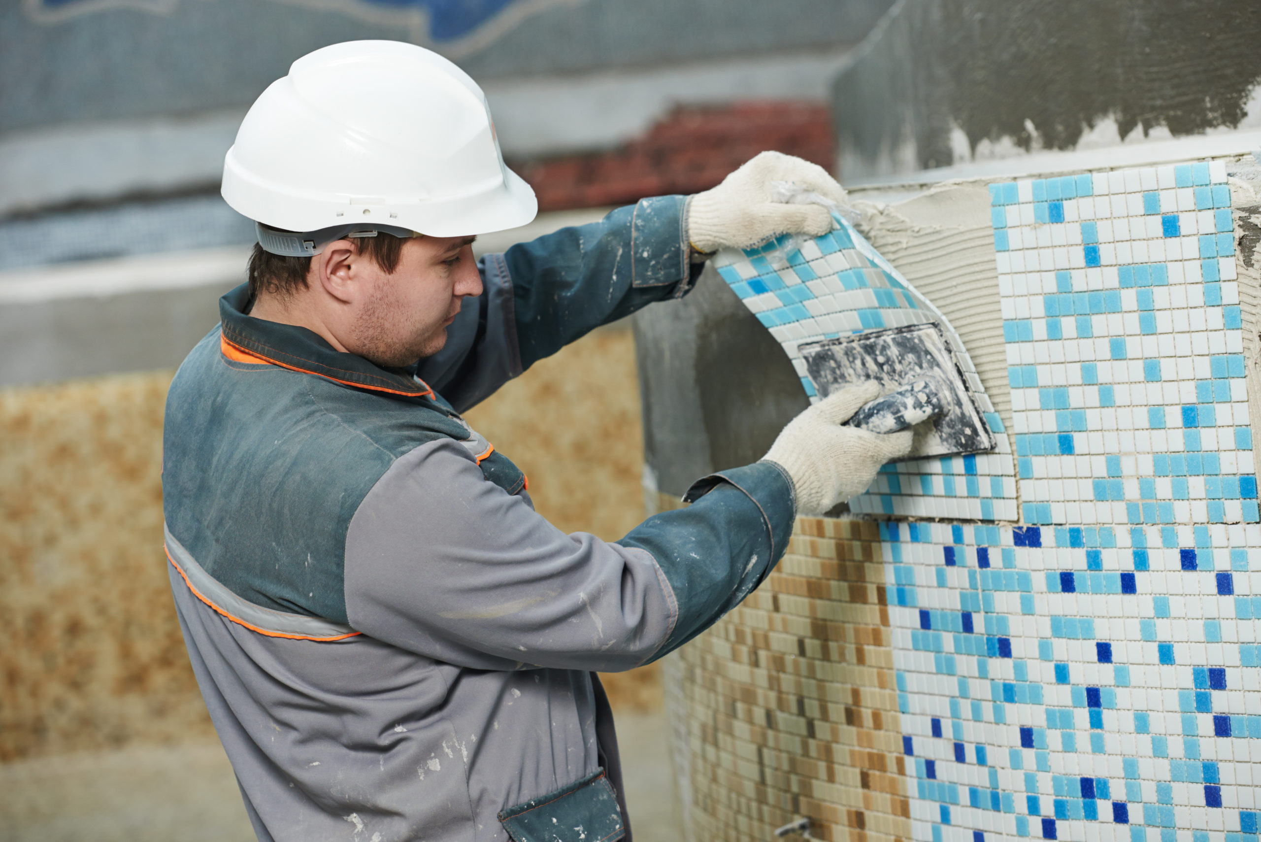 A man carefully installing wall tiles for a pool, ensuring precise placement to enhance the pool's aesthetic appeal and durability.