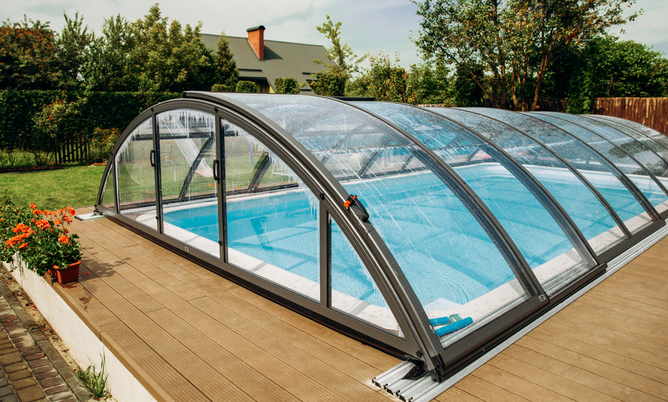 A pool enclosed by transparent glass walls and ceiling, allowing for unobstructed views of the surrounding landscape while providing shelter and climate control for year-round enjoyment.