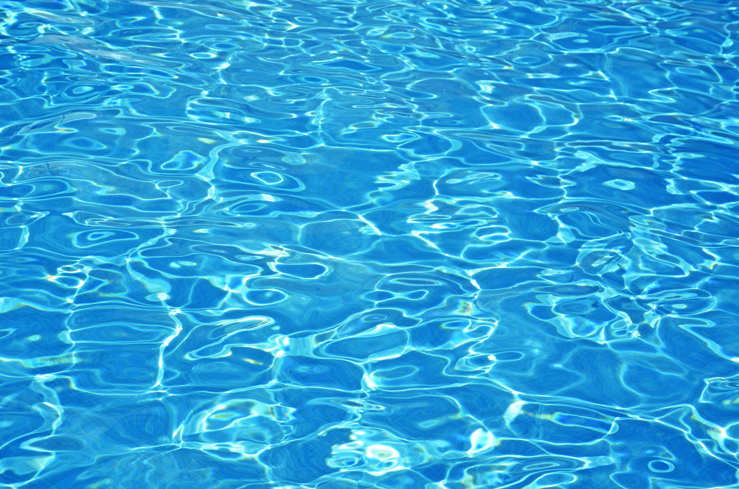 Sparkling pool water under the glistening sunlight, with rippling waves and a crystal-clear surface, inviting for a refreshing swim on a bright and sunny day.