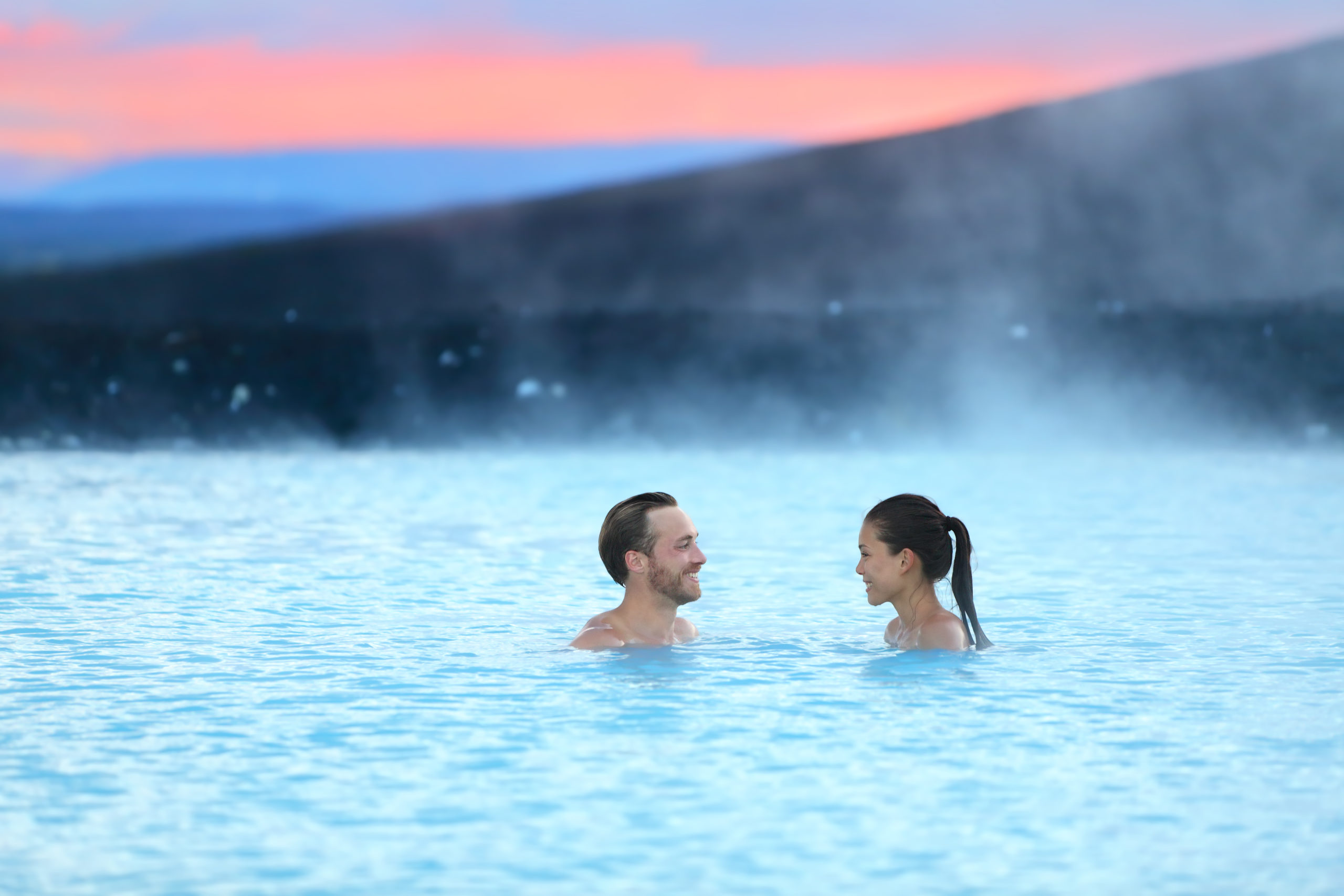 A couple relaxing in a natural hot spring, surrounded by rustic and untouched natural beauty, enjoying a warm soak in the geothermal waters.