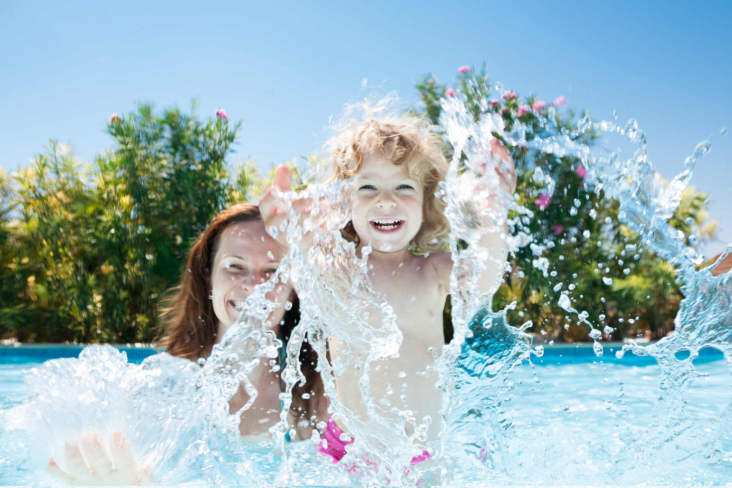 A baby and its mother joyfully splashing water in a pool, sharing a playful and bonding moment of fun and laughter.